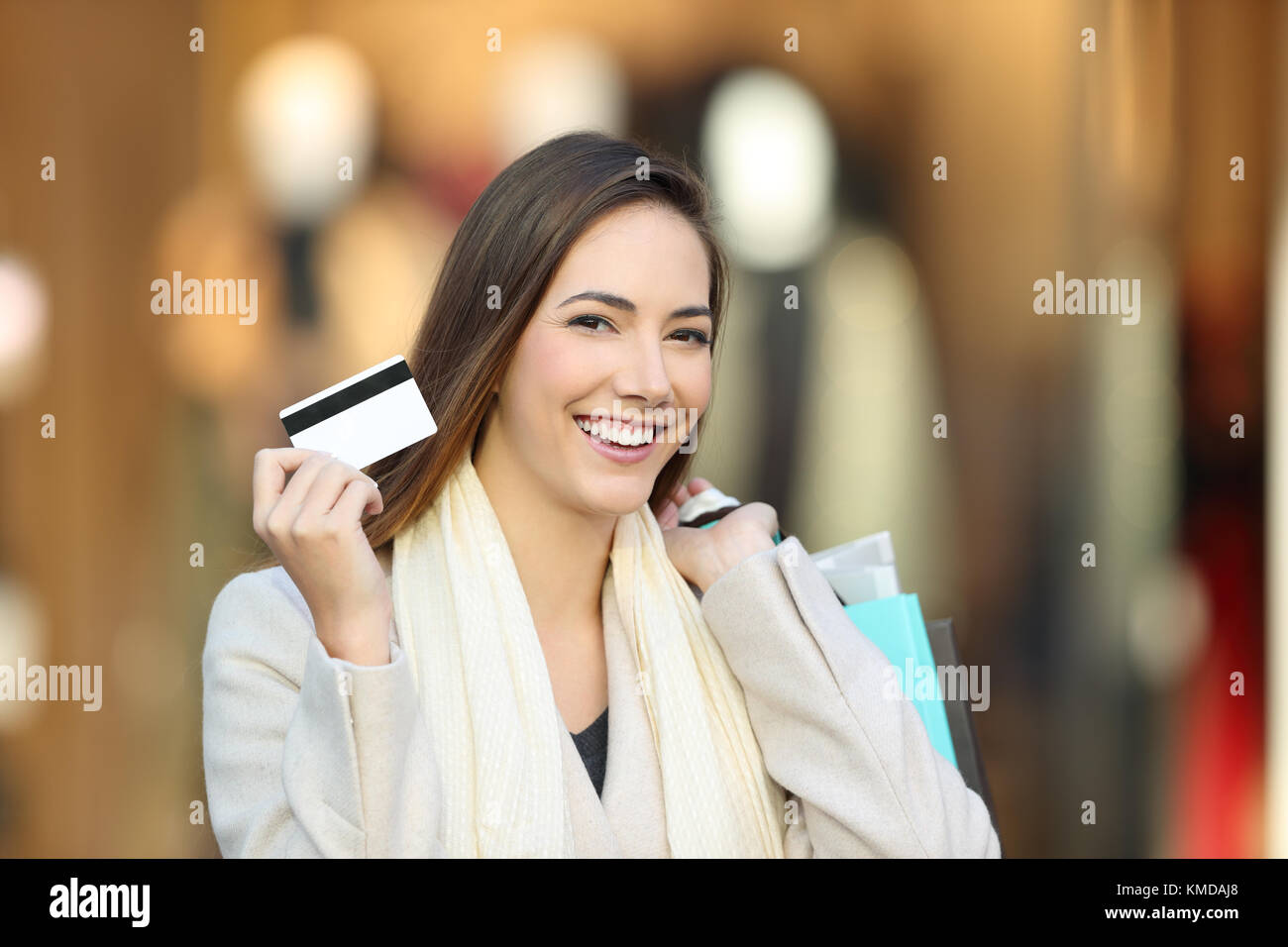 Happy shopper che indossa un mantello bianco shopping e che mostra la carta di credito in un centro commerciale interno Foto Stock