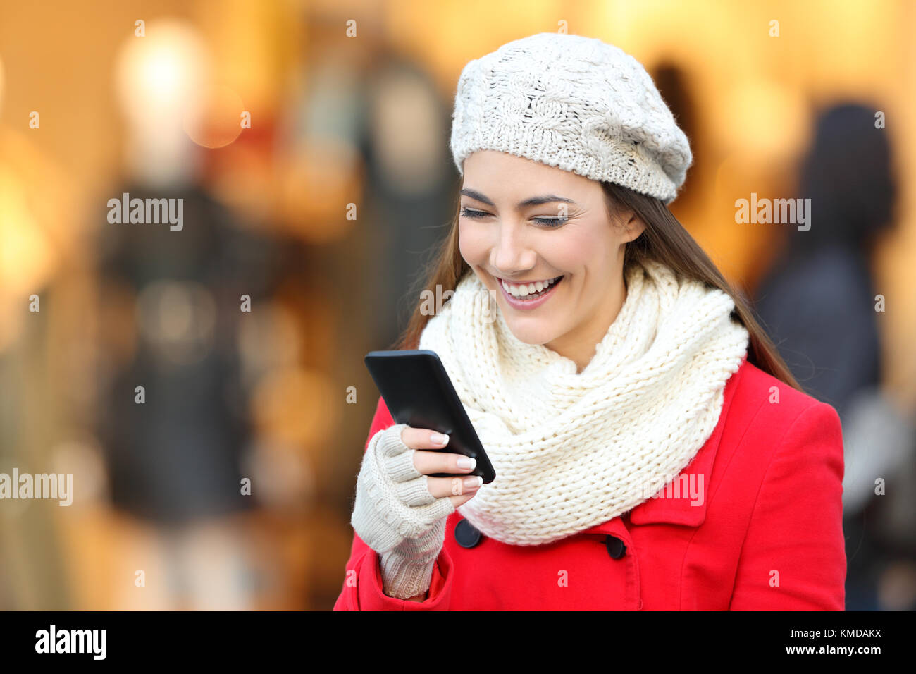 Ritratto di una donna felice indossando cappotto rosso smart di lettura del contenuto del telefono in un centro commerciale in inverno Foto Stock