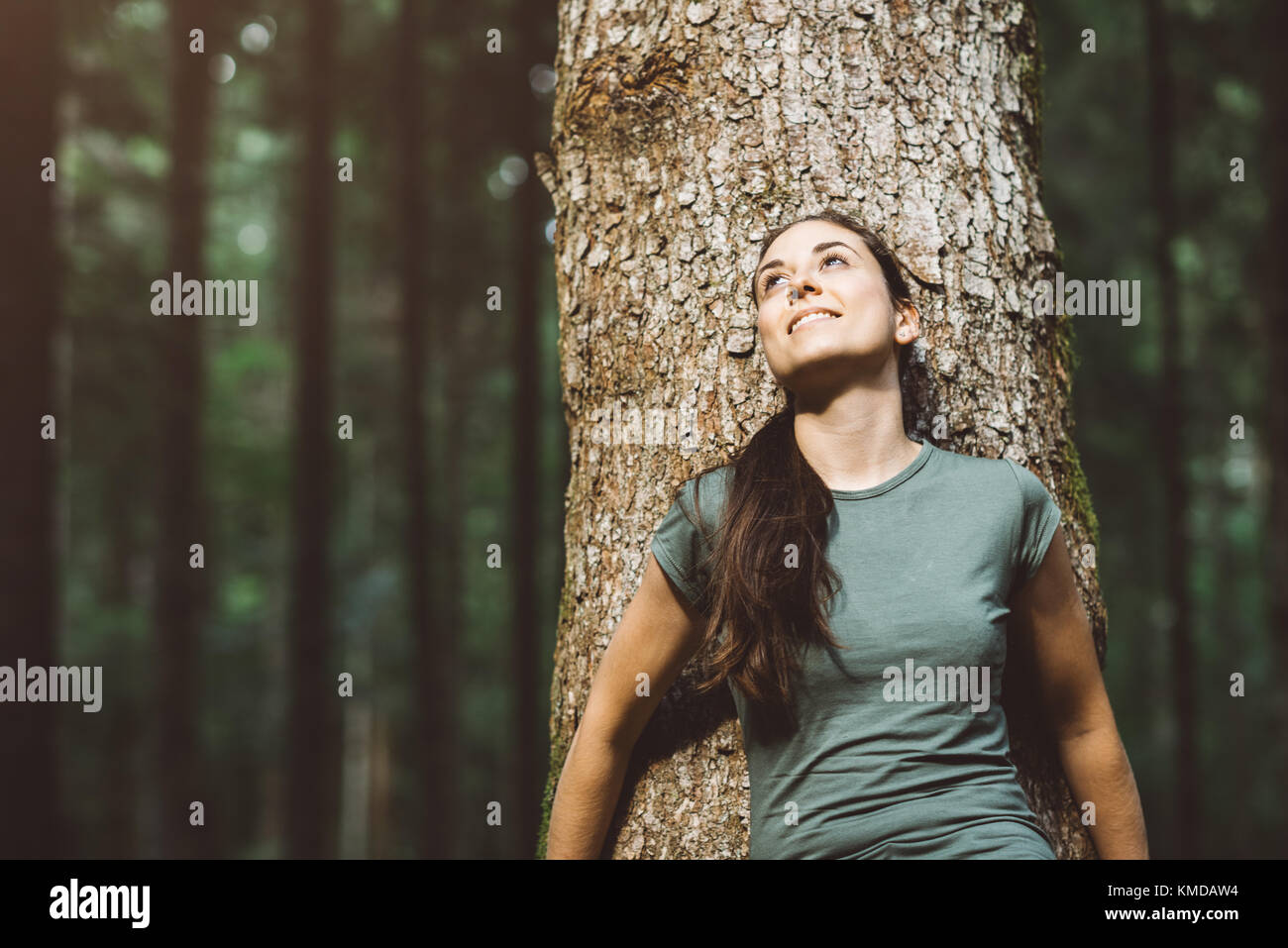Donna sorridente e rilassarsi nella natura, ella è appoggiato su di un albero e guardando lontano Foto Stock