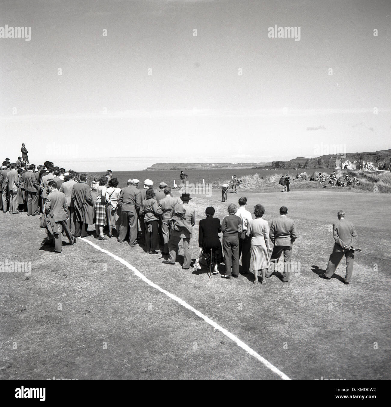 1951, storico, vista del Royal Portrush Golf Club sulla costa di Antrim, Irlanda del Nord, che quest'anno sta tenendo il torneo di golf Briitsh Open e vediamo spettatori ben vestiti in piedi intorno a un verde costiero per guardare il putt golfers. Ora noto come semplicemente 'The Open', questo evento è stato vinto dal golfista inglese Max Faulkner, la sua vittoria unica maggiore. Foto Stock