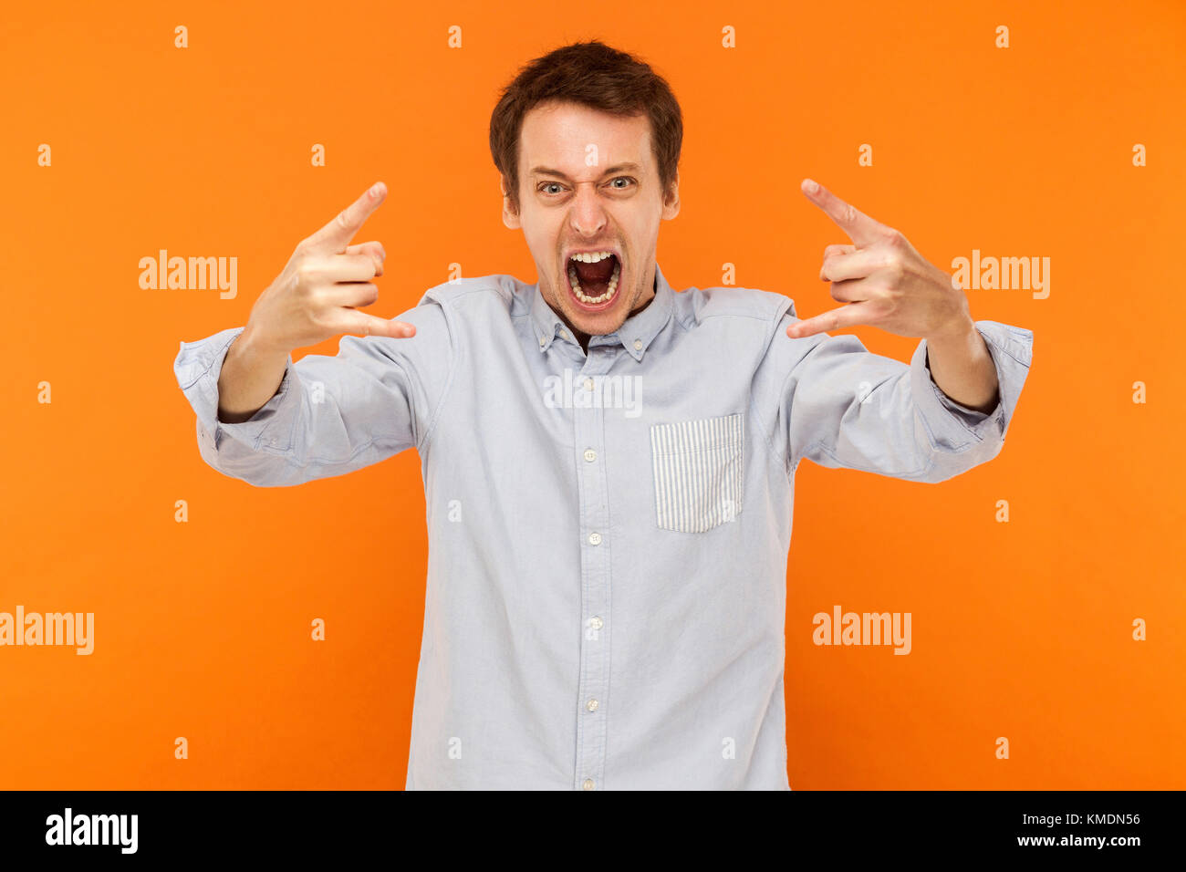 Rock and Roll! Uomo espressiva che mostra rock mano alla fotocamera e gridare. Studio shot, sfondo arancione Foto Stock