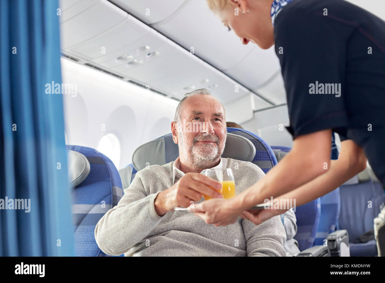 Assistente di volo che serve succo d'arancia all'uomo in aereo Foto Stock