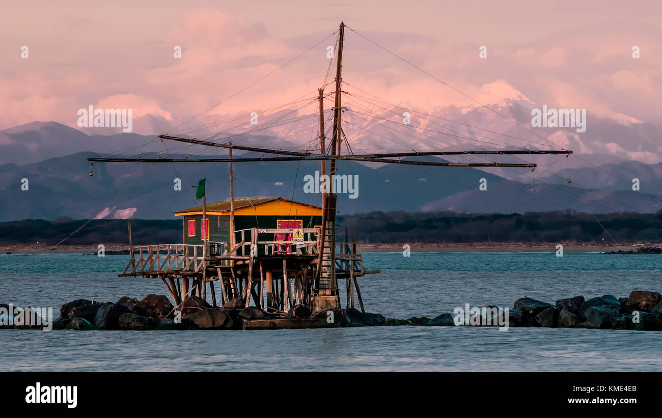 Interrompi Net Capanna di pesca al tramonto contro le Alpi con neve, Marina di Pisa, Toscana, Italia Foto Stock