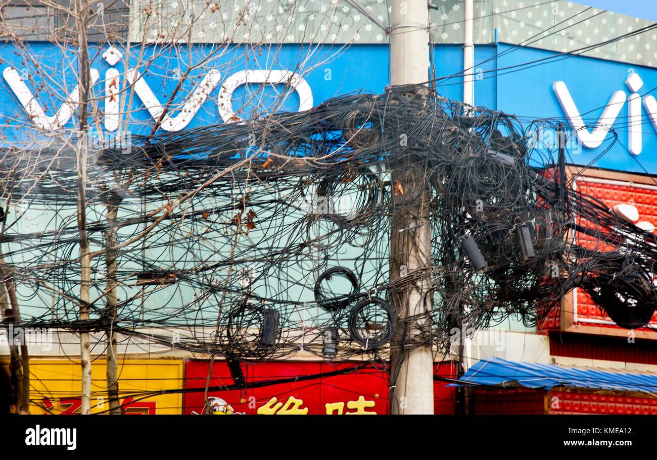 Un pasticcio aggrovigliato di cavi elettrici e telefonici alti pali attraverso gran parte di Xian centrale, dando luogo a domande re efficiente amministrazione di utilità, distribuzione, e riparazione in questa parte del nord-est della Cina.Xi'an, precedentemente romanizzato come Sian, e anche conosciuto come Chang'an prima della dinastia Ming, è la capitale della provincia di Shaanxi, Repubblica popolare di Cina.IT è La più antica delle quattro grandi capitali antiche, avendo mantenuto la posizione sotto molte delle dinastie più importanti nella storia cinese, tra cui Zhou occidentale, Qin, Han occidentale, sui, e Tang. Foto Stock