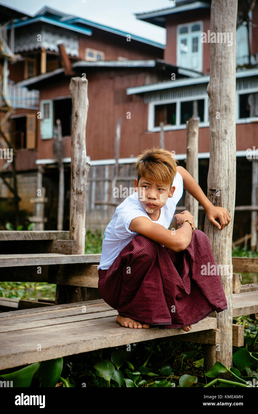 Ragazzo accovacciato sul molo, Lago Inle, Myanmar Foto Stock