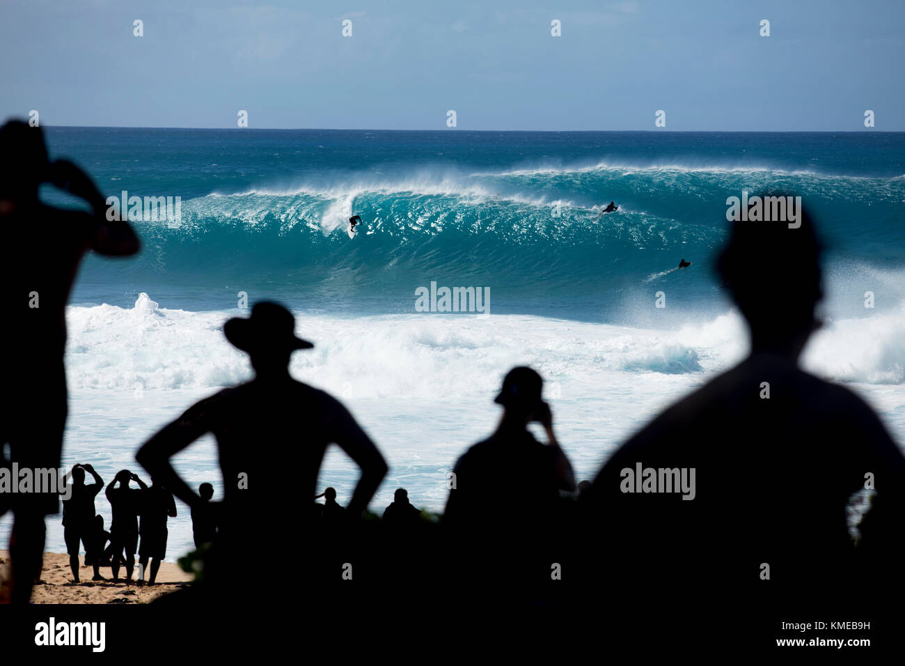 Spettatori dalle silhouette che guardano i surfisti che cavalcano onde enormi a fama mondiale Gasdotto Banzai, sulla sponda nord di Oahu, Hawaii, USA Foto Stock