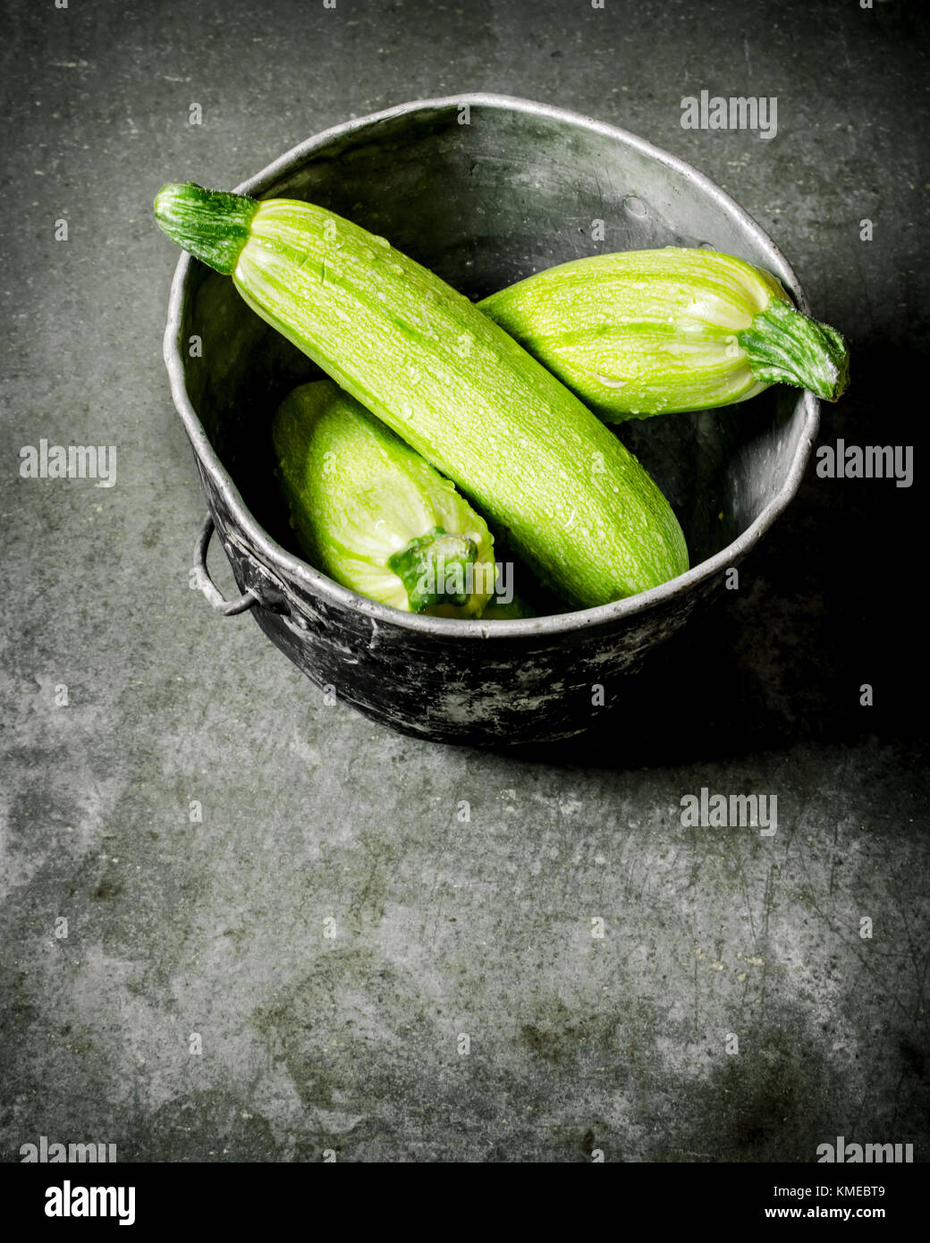 Zucchine fresche nella vecchia pentola. su un sfondo di pietra. Foto Stock