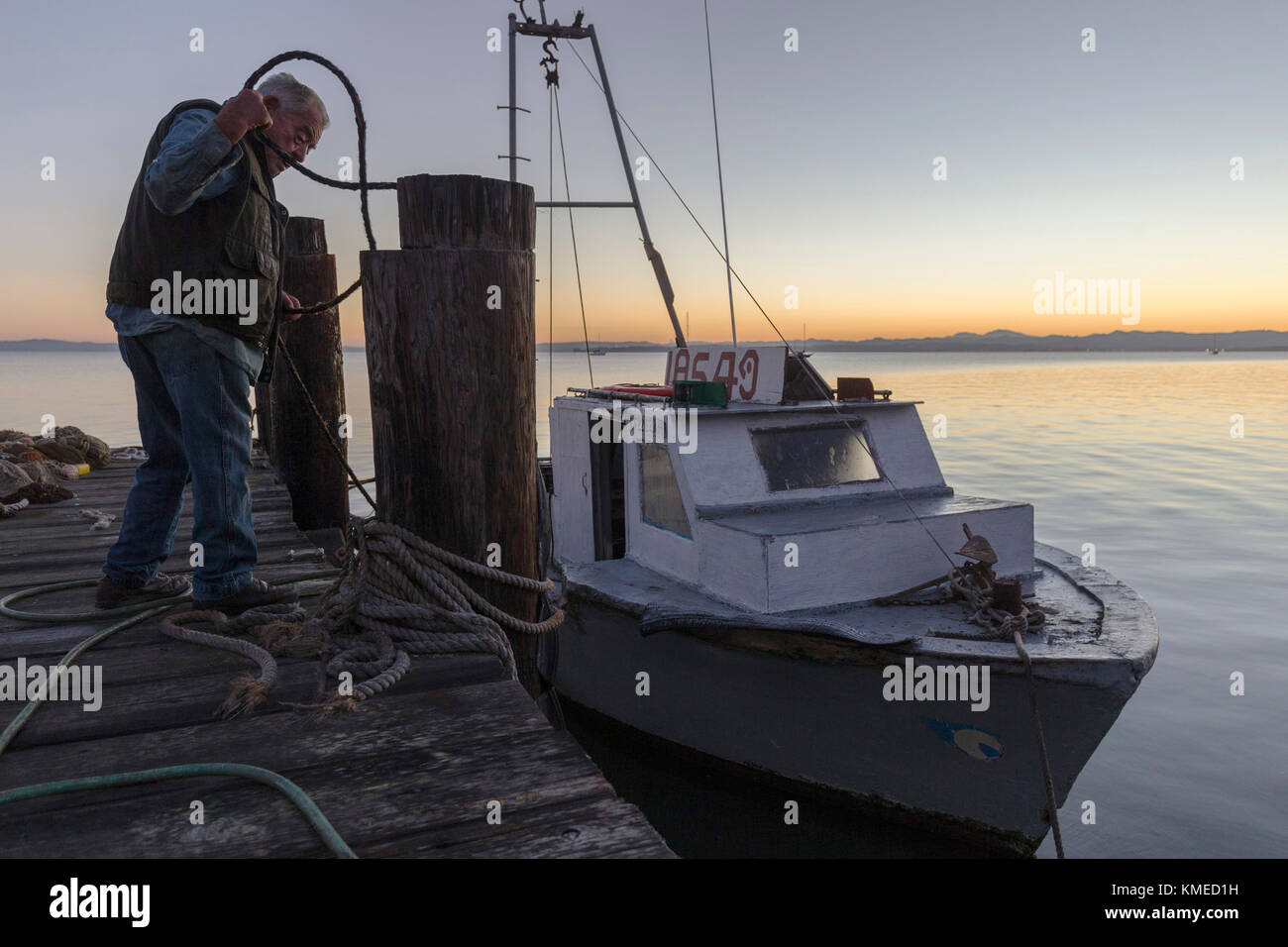 Pescatore di gamberetti in piedi sul molo vicino a barca al tramonto,Cina Camp,California , Stati Uniti Foto Stock