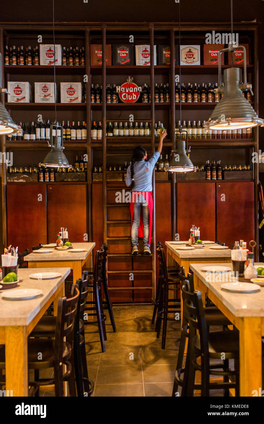 Donna tirando verso il basso la bottiglia di rum a Central de Cevicheria, ristorante a Bogotà, Colombia Foto Stock