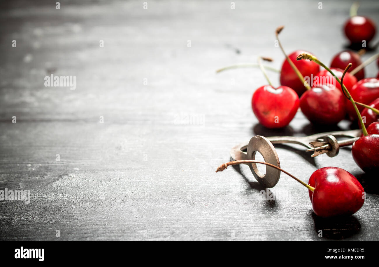 Rosso ciliegia con un utensile di metallo di ciliegia. su un nero lo sfondo di legno. Foto Stock