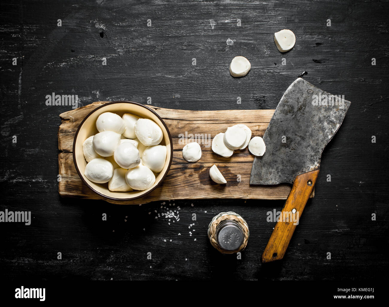 Mozzarella fresca con un ascia per tagliare. su un nero lo sfondo di legno. Foto Stock