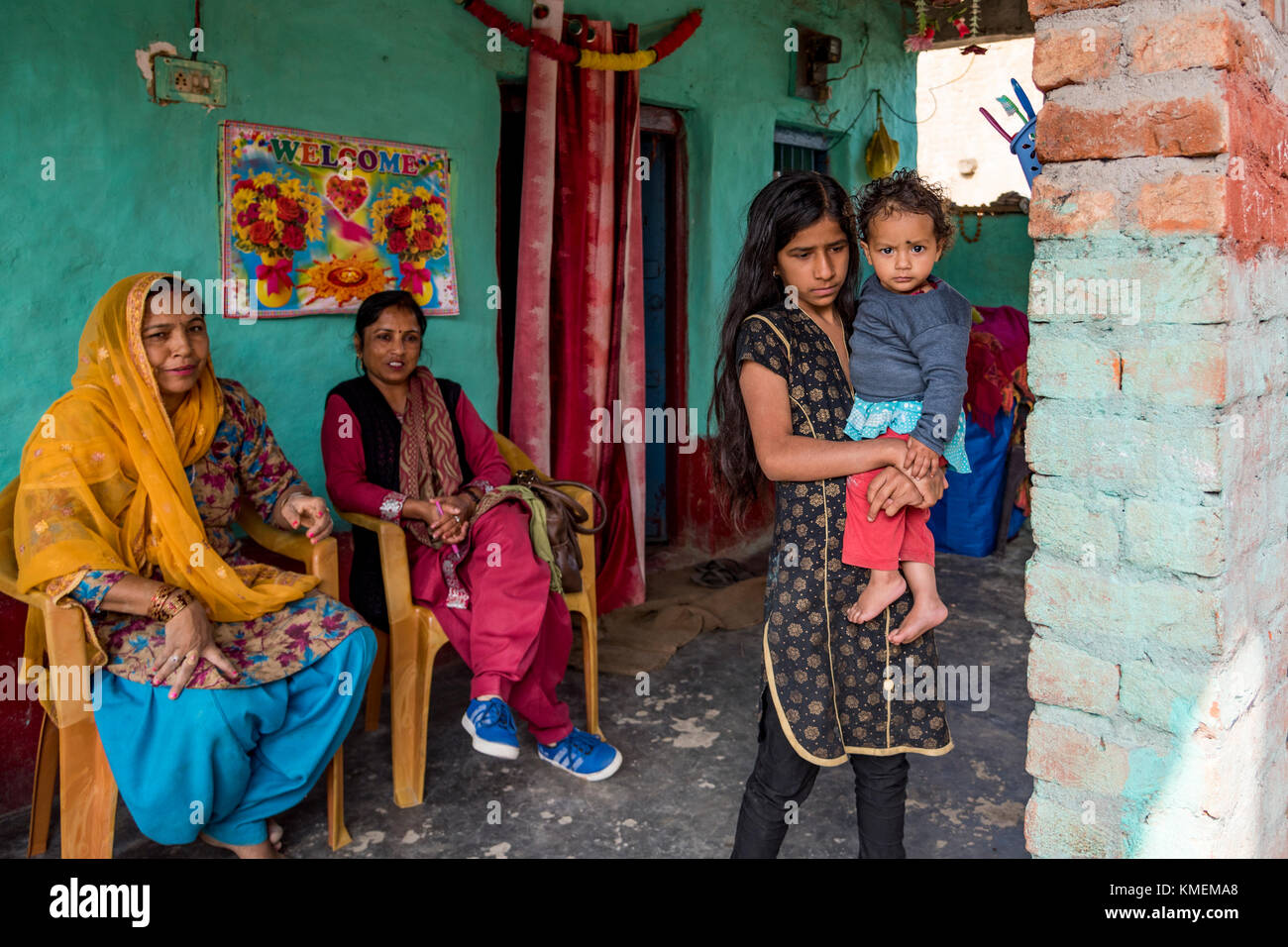 Una famiglia indiana seduto in casa loro con una giovane ragazza con un bimbo tra le braccia. Foto Stock