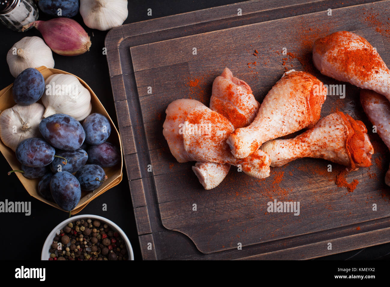 Primo piano della materie cosce di pollo con l'aglio, la paprika, il sale e il pepe miscela su uno sfondo scuro. vista dall'alto. intorno al bordo di taglio anche gli scalogni e Foto Stock