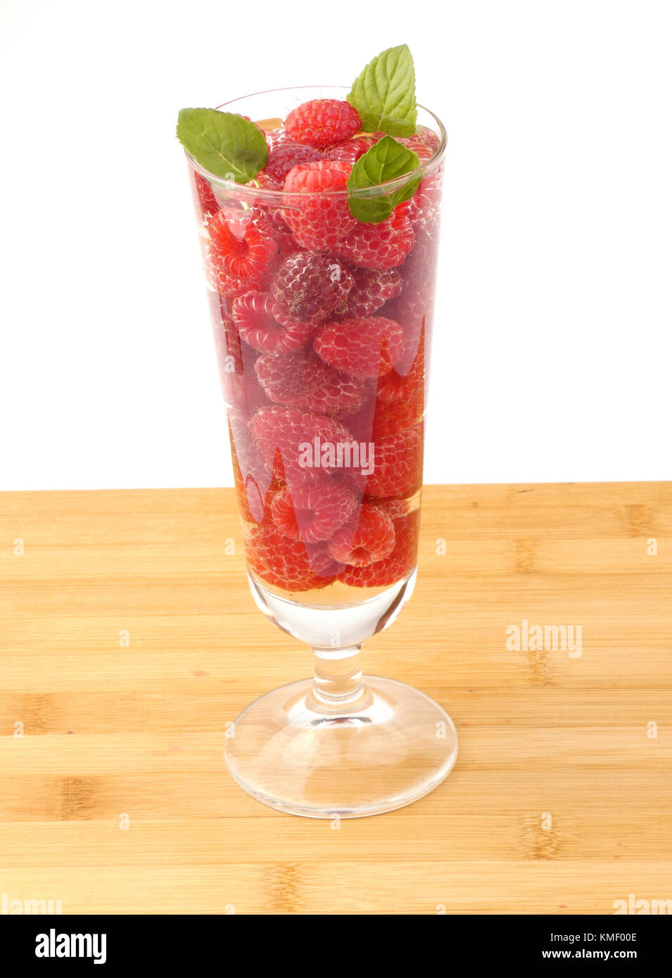 Bicchiere d'acqua pieno con lamponi isolati su tavola in legno Foto Stock