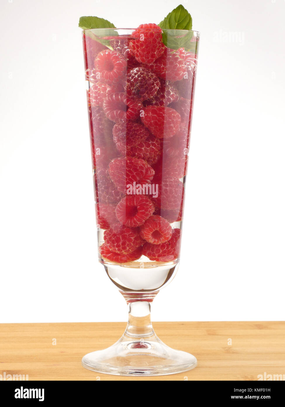 Bicchiere d'acqua pieno con lamponi isolati su tavola in legno Foto Stock