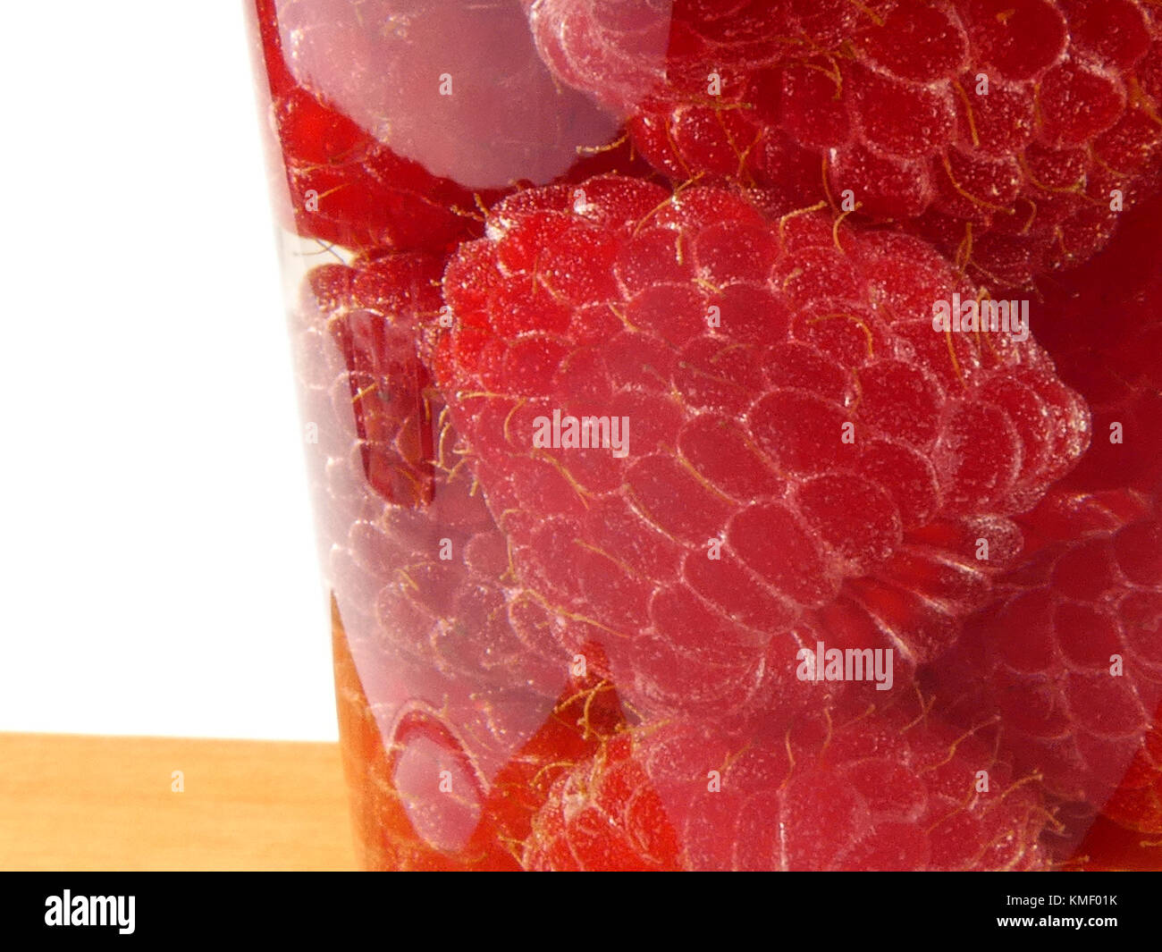 Bicchiere d'acqua pieno con lamponi isolati su tavola in legno Foto Stock