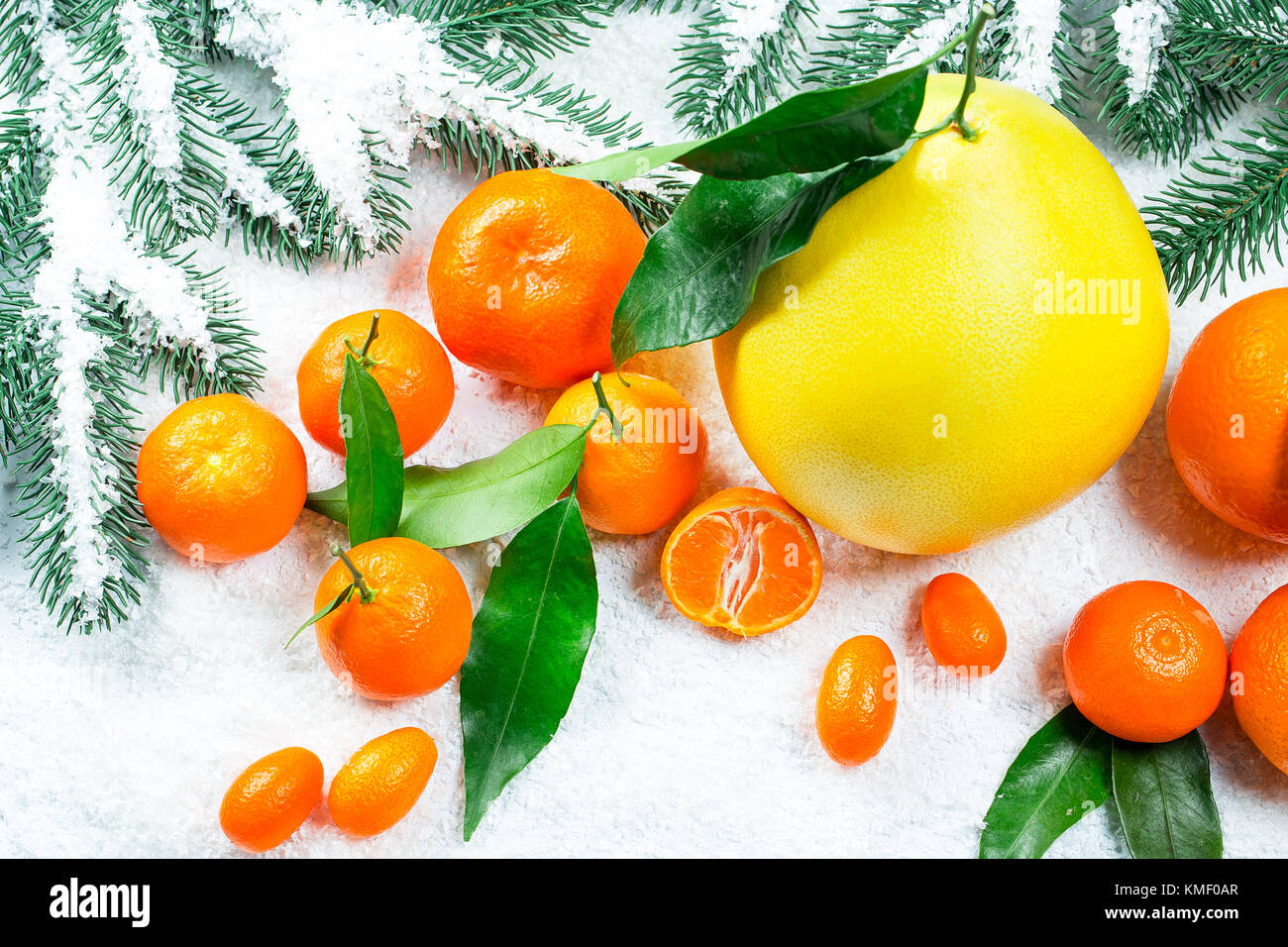 I mandarini freschi, arance, pomelo, kumquat, kinkan con foglie sul bianco della neve. mature agrumi sfondo. simbolo del nuovo anno e di natale Foto Stock