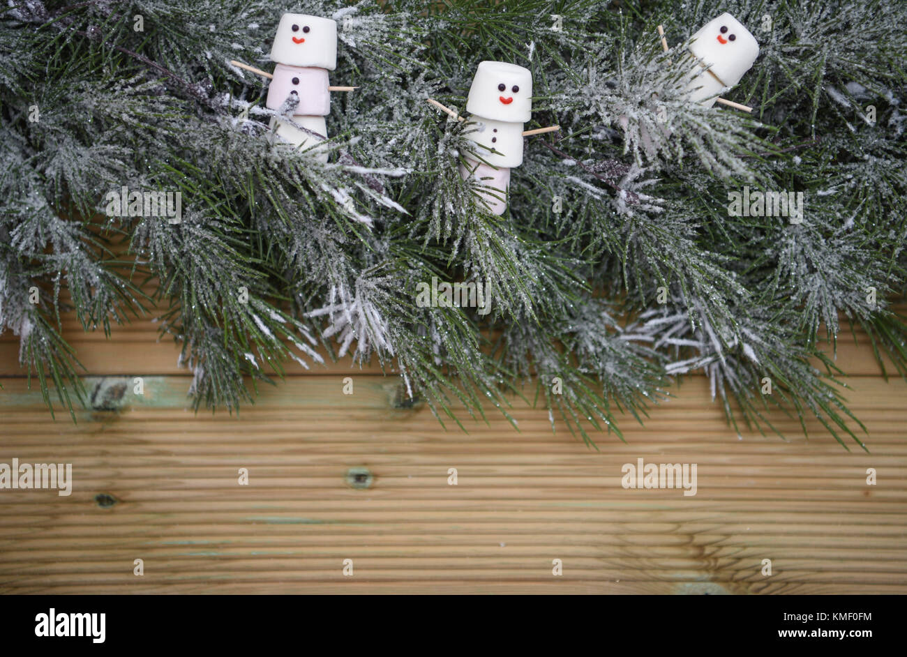 Natale immagine di fotografia con tree garland cosparsi di neve su rustiche in legno naturale con sfondo spazio copia e marshmallows a forma di pupazzo di neve Foto Stock