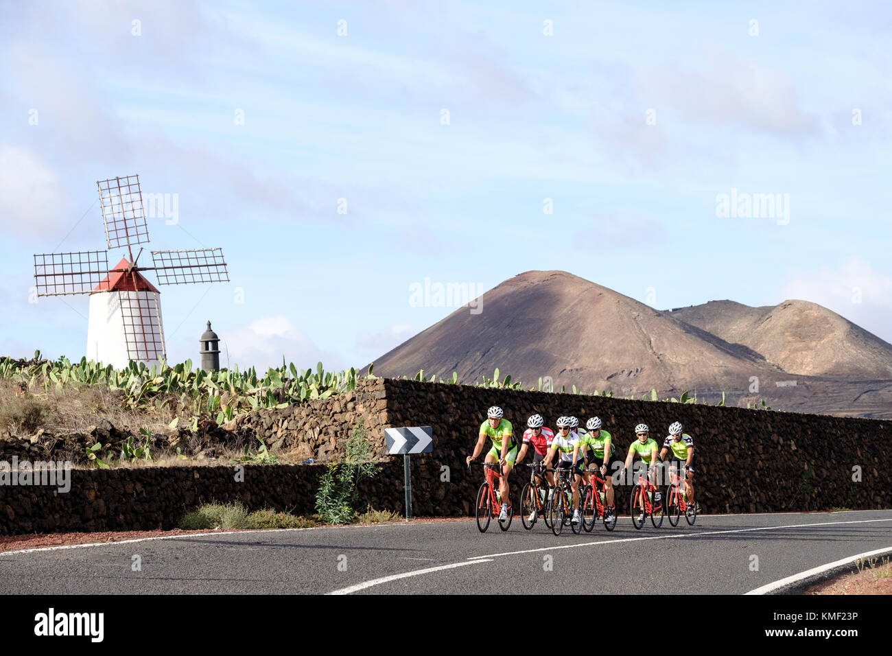 Un gruppo di ciclisti a pedalare su strada con i vulcani e il mulino a vento in background,Lanzarote,isole Canarie,Spagna Foto Stock
