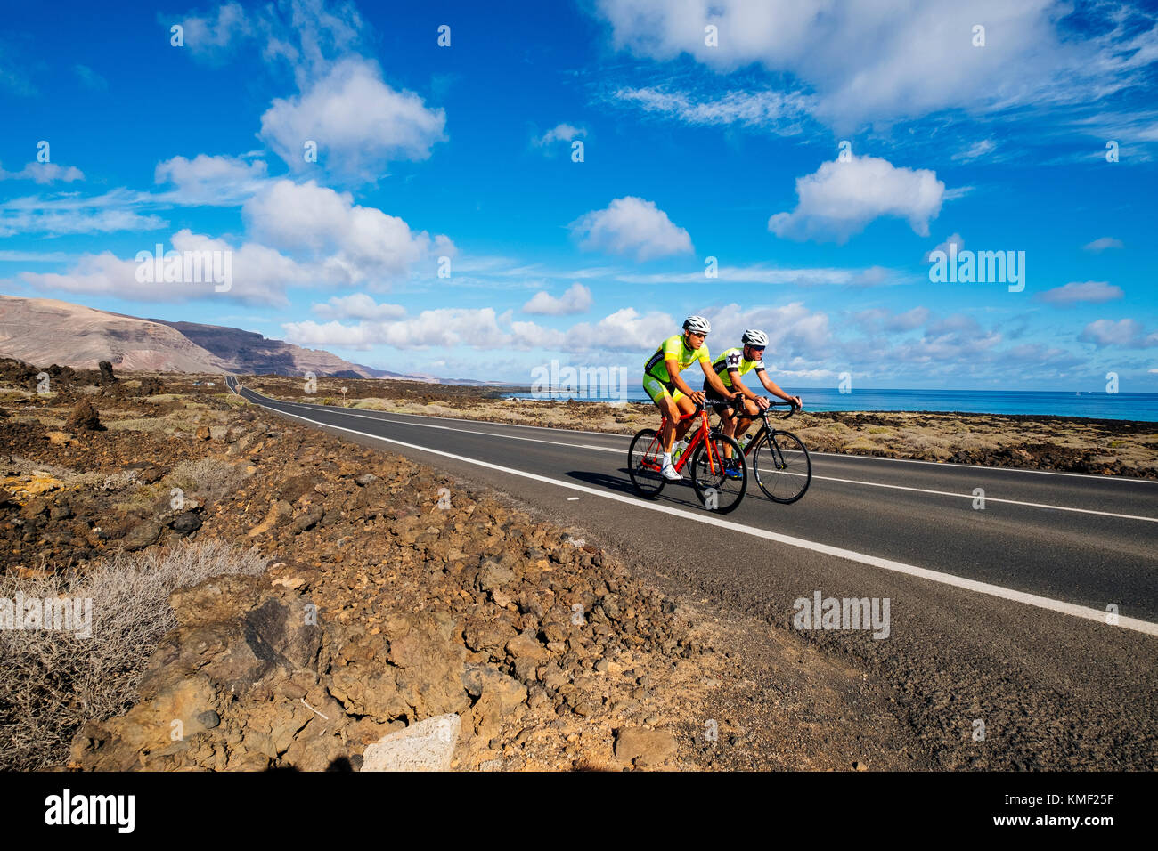 Due ciclisti su strada in sella a fianco a fianco sulla strada vicino alla costa, Lanzarote, Isole Canarie, Spagna Foto Stock