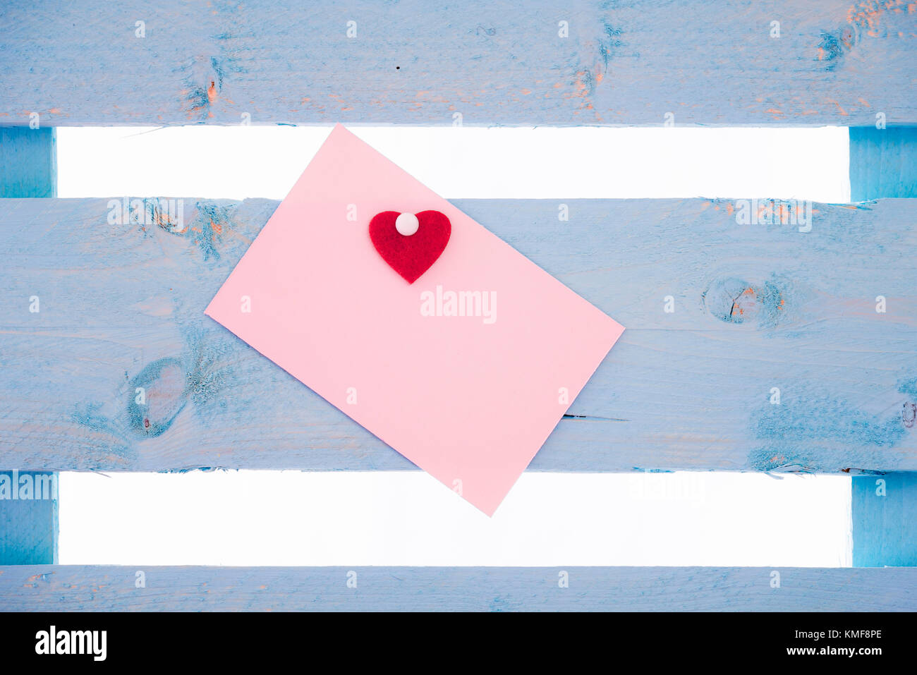 Vuoto carta rosa nota con un cuore rosso incollate e insieme imperniato ad un blu staccionata in legno. Foto Stock