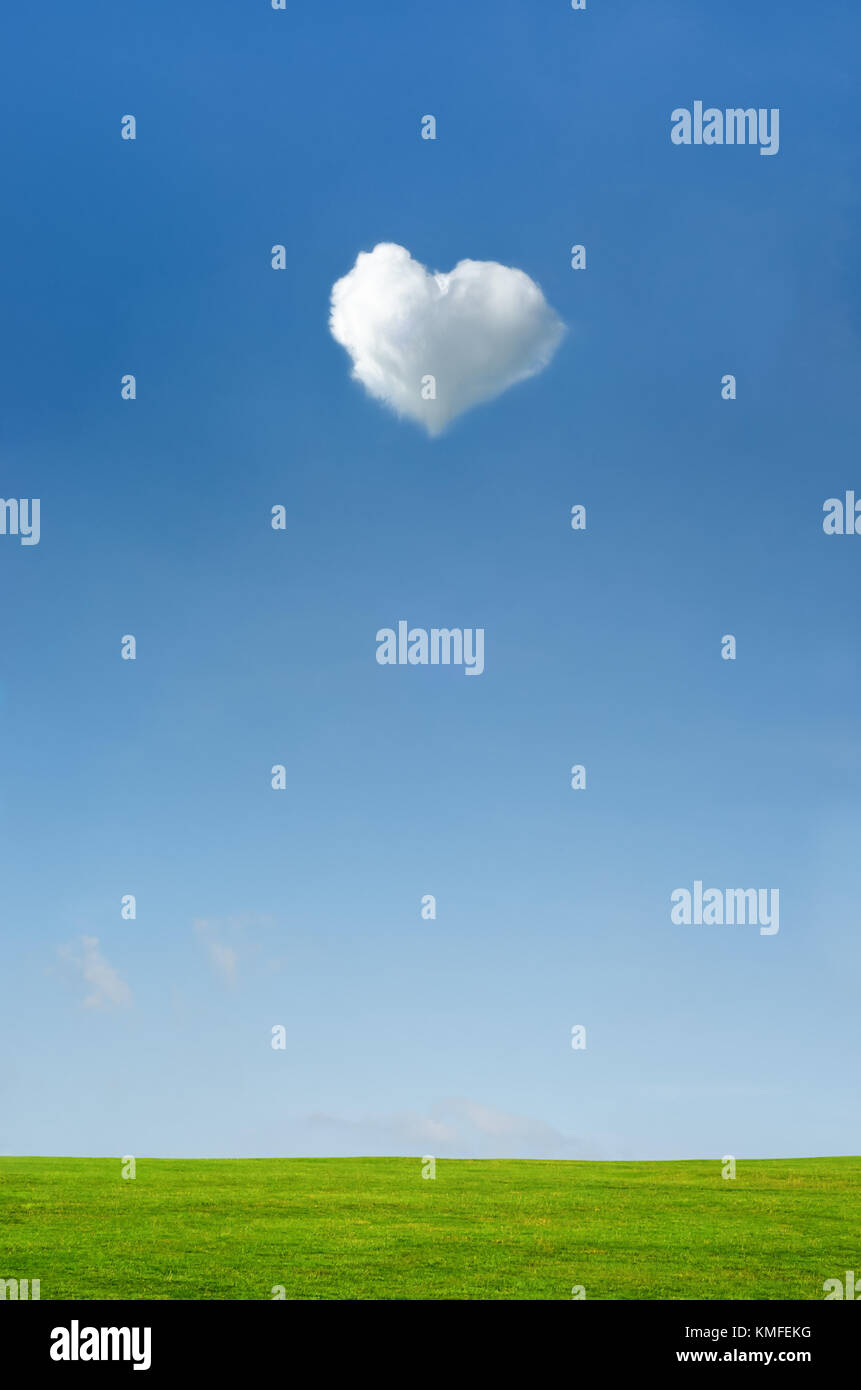 A forma di cuore bianco soffice nuvola impostato in un luminoso cielo blu con erba verde paesaggio di campagna sottostante. Foto Stock