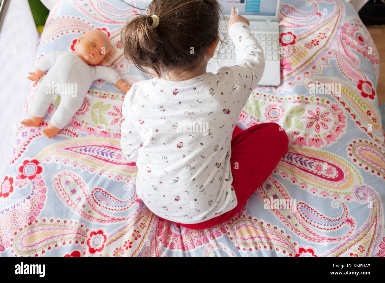 Poco ragazza seduta nel letto e giocare online con il computer portatile. Ella sta toccando lo schermo Foto Stock