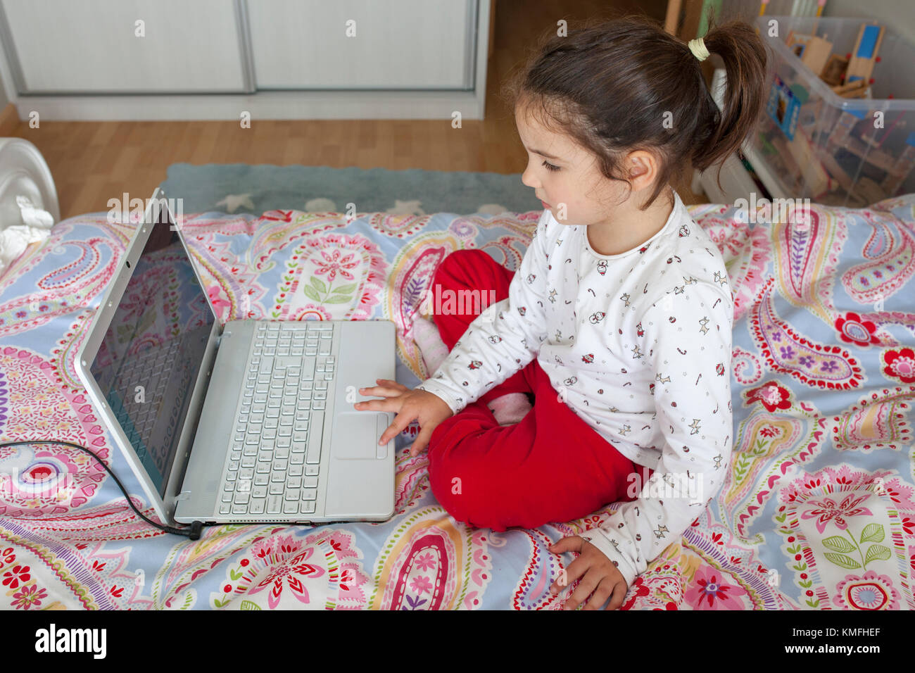 Poco ragazza seduta nel letto e giocare ai videogame on line nella sua camera da letto Foto Stock