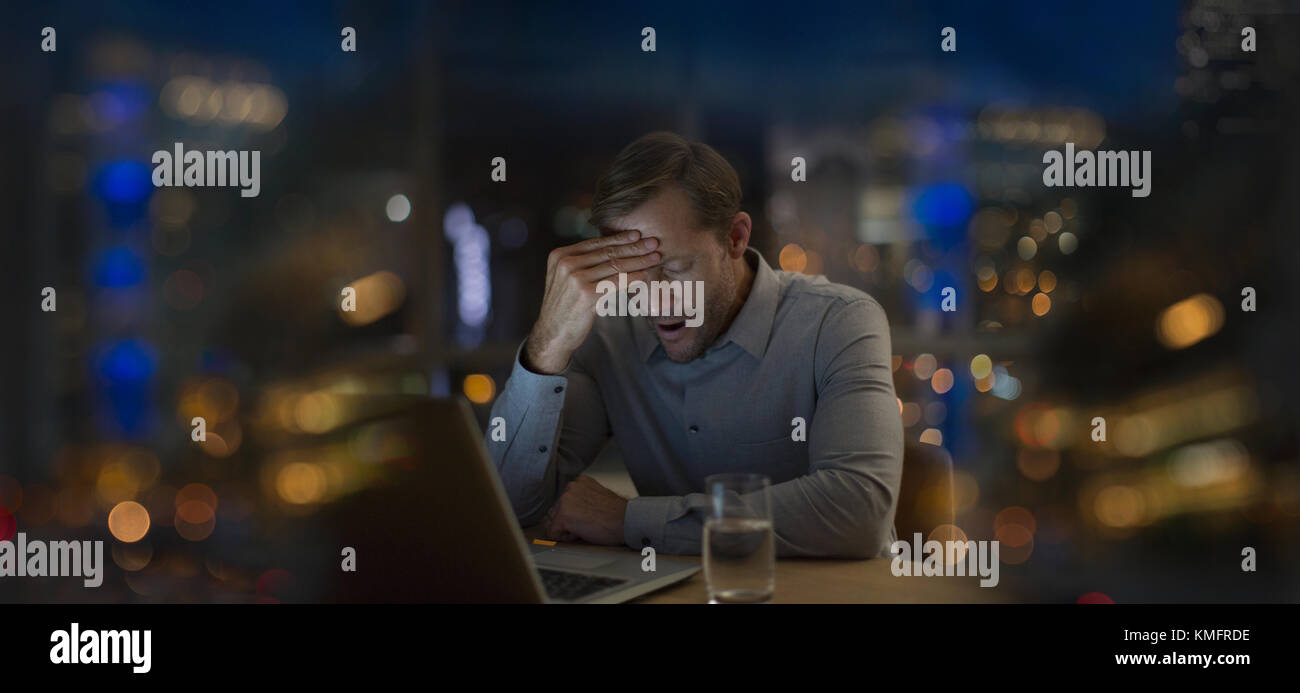 Uomo d'affari stanco che urla con la testa nelle mani, lavorando tardi in ufficio di notte Foto Stock