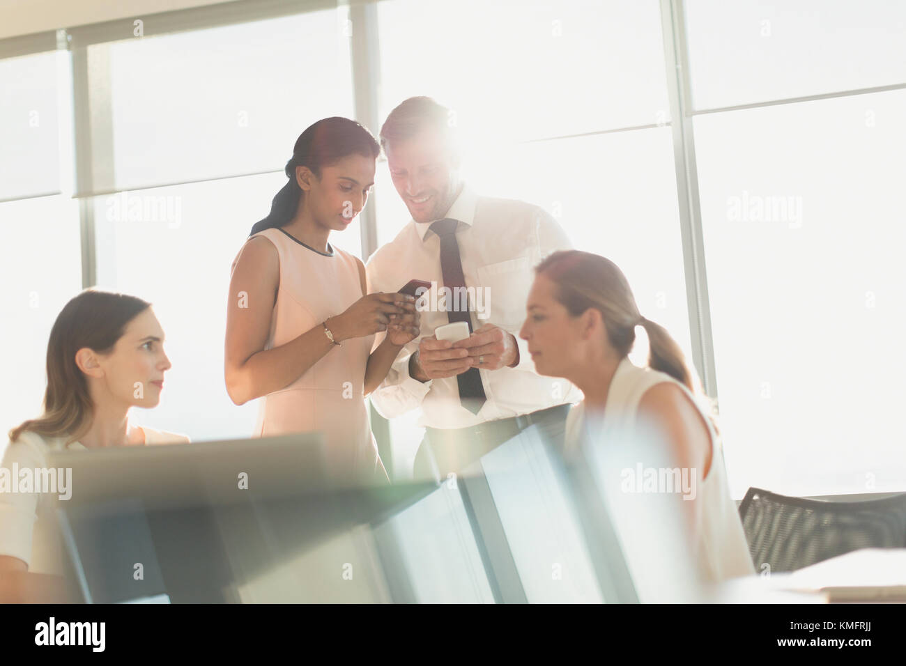 Gli uomini d'affari che si sono posti con i telefoni cellulari nella soleggiata sala conferenze riunione Foto Stock