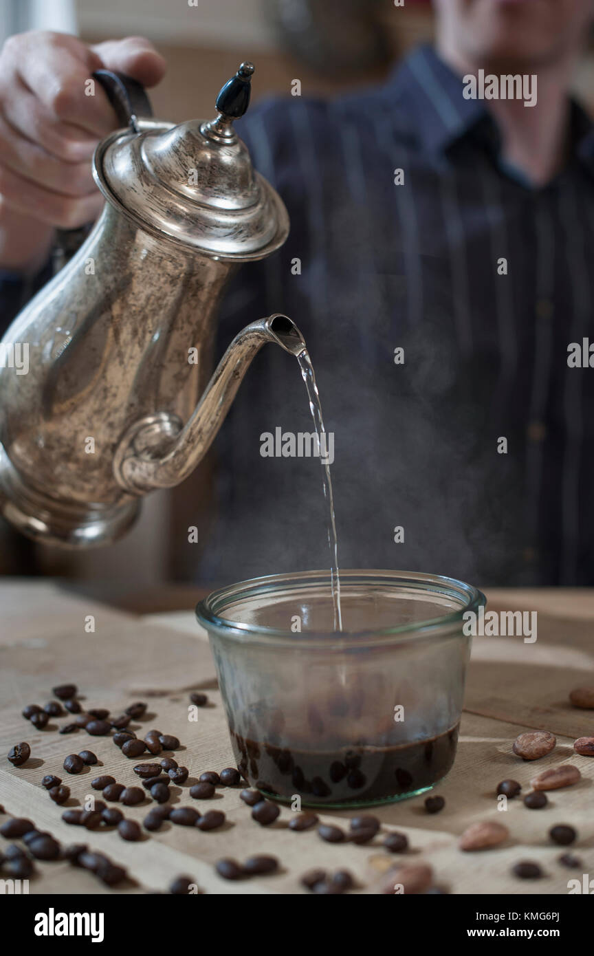 L'uomo versando acqua calda in un bicchiere con la polvere di caffè Foto Stock