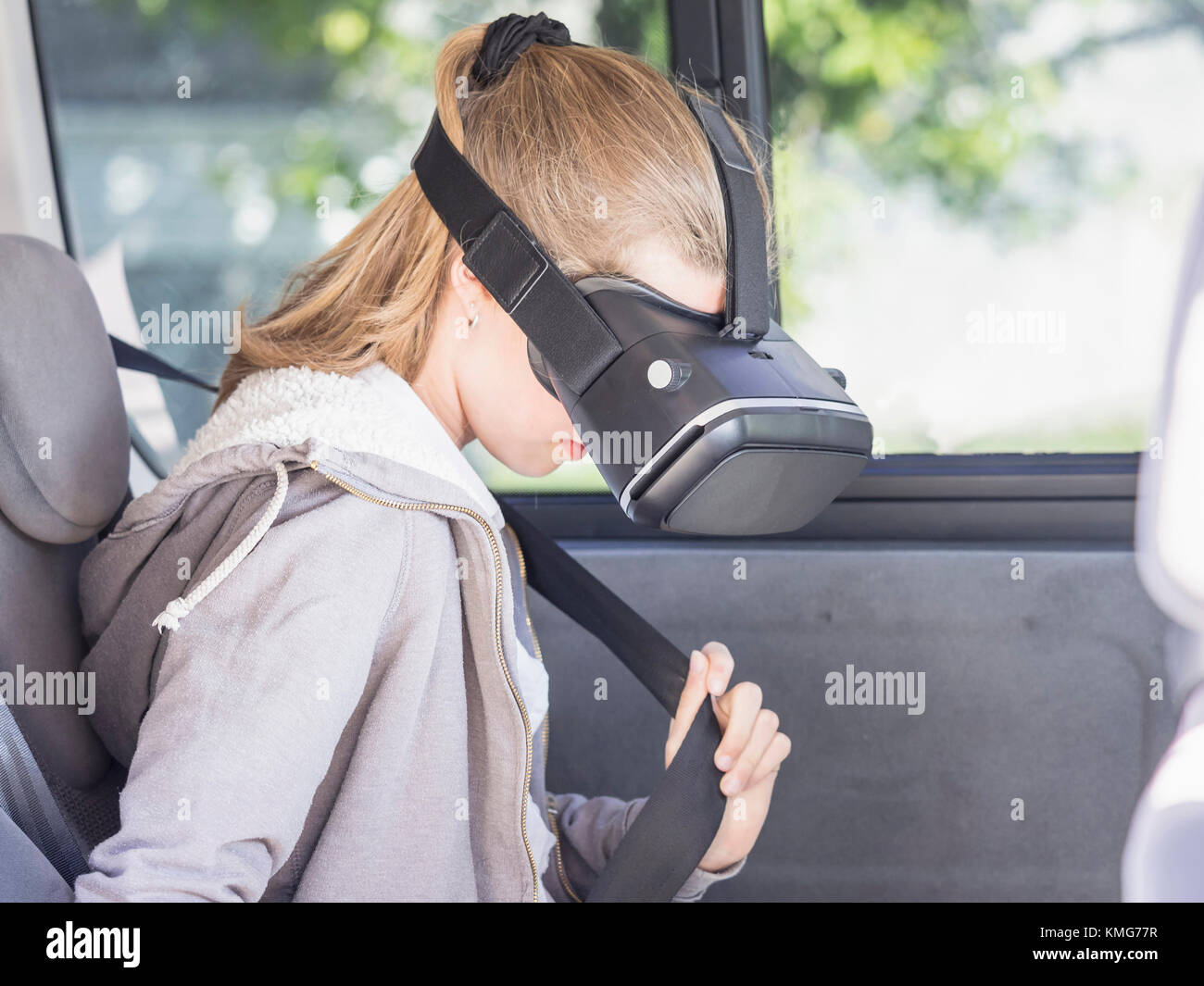 Ragazza che usa la cuffia per la realtà virtuale durante la regolazione della cintura di sicurezza dell'auto Foto Stock