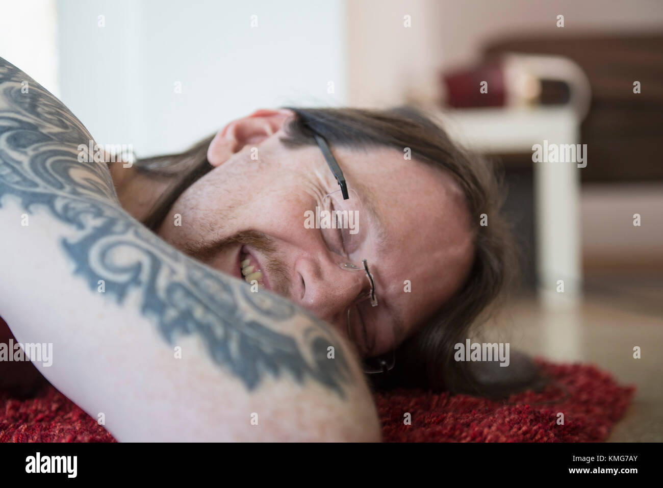 Uomo tatuato con gli occhi chiusi che si rilassa sul tappeto a casa Foto Stock