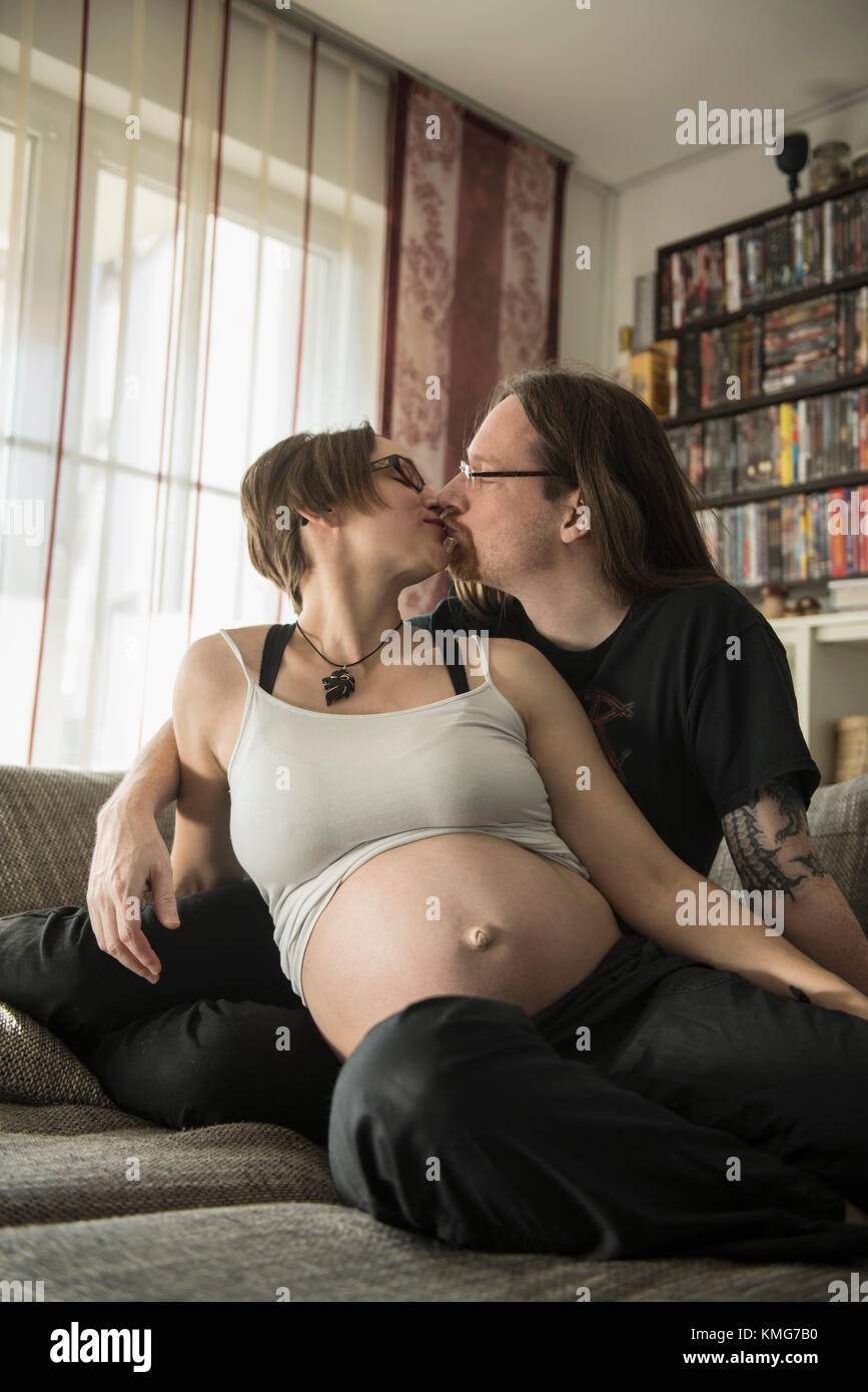 Una coppia incinta che si baciava sul divano Foto Stock