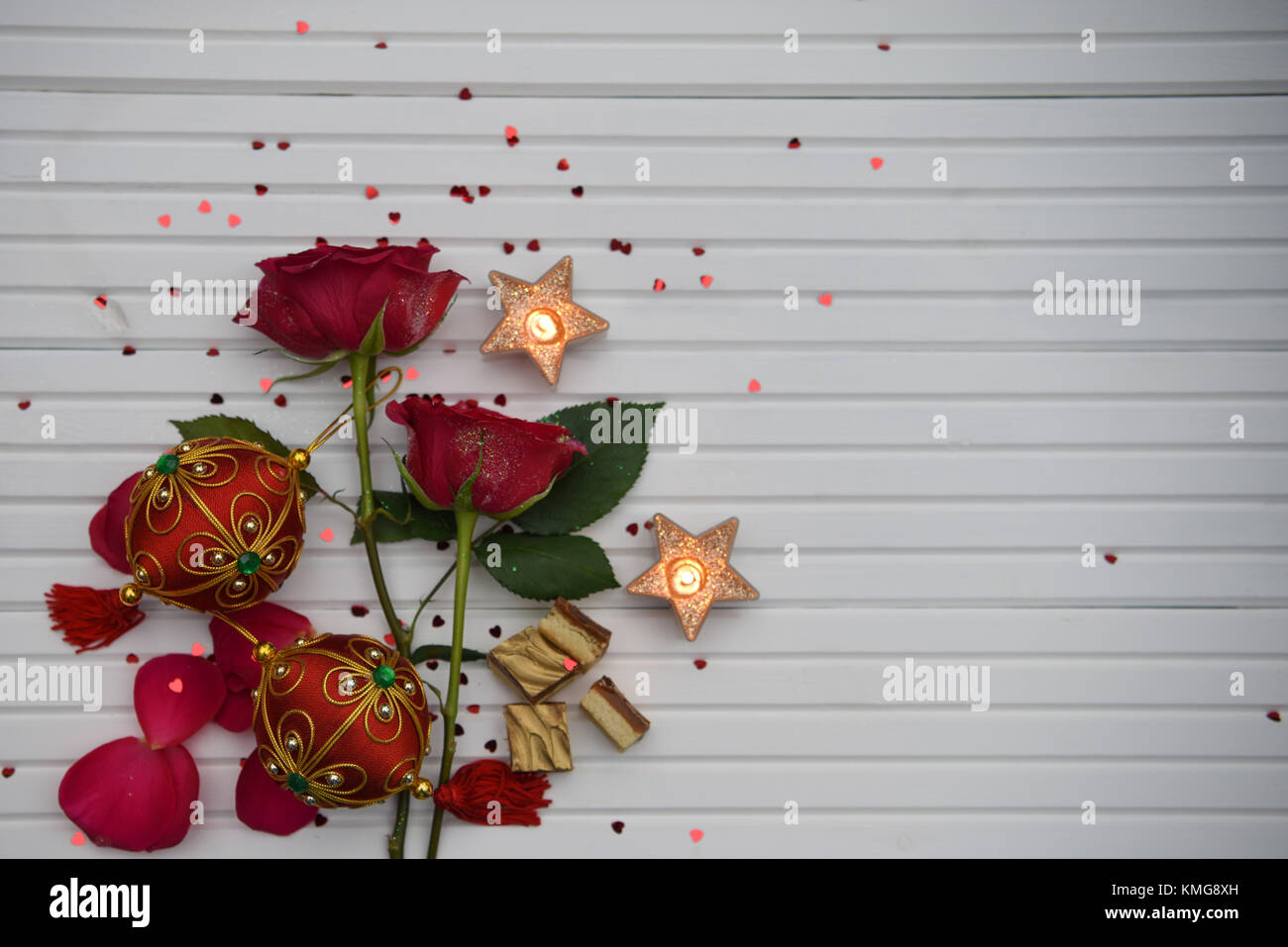 Christmas Romantic cibo fotografia immagine con rose rosse fiori candele accese e rosso verde ninnolo decorazione bianco su uno sfondo di legno con spazio di copia Foto Stock