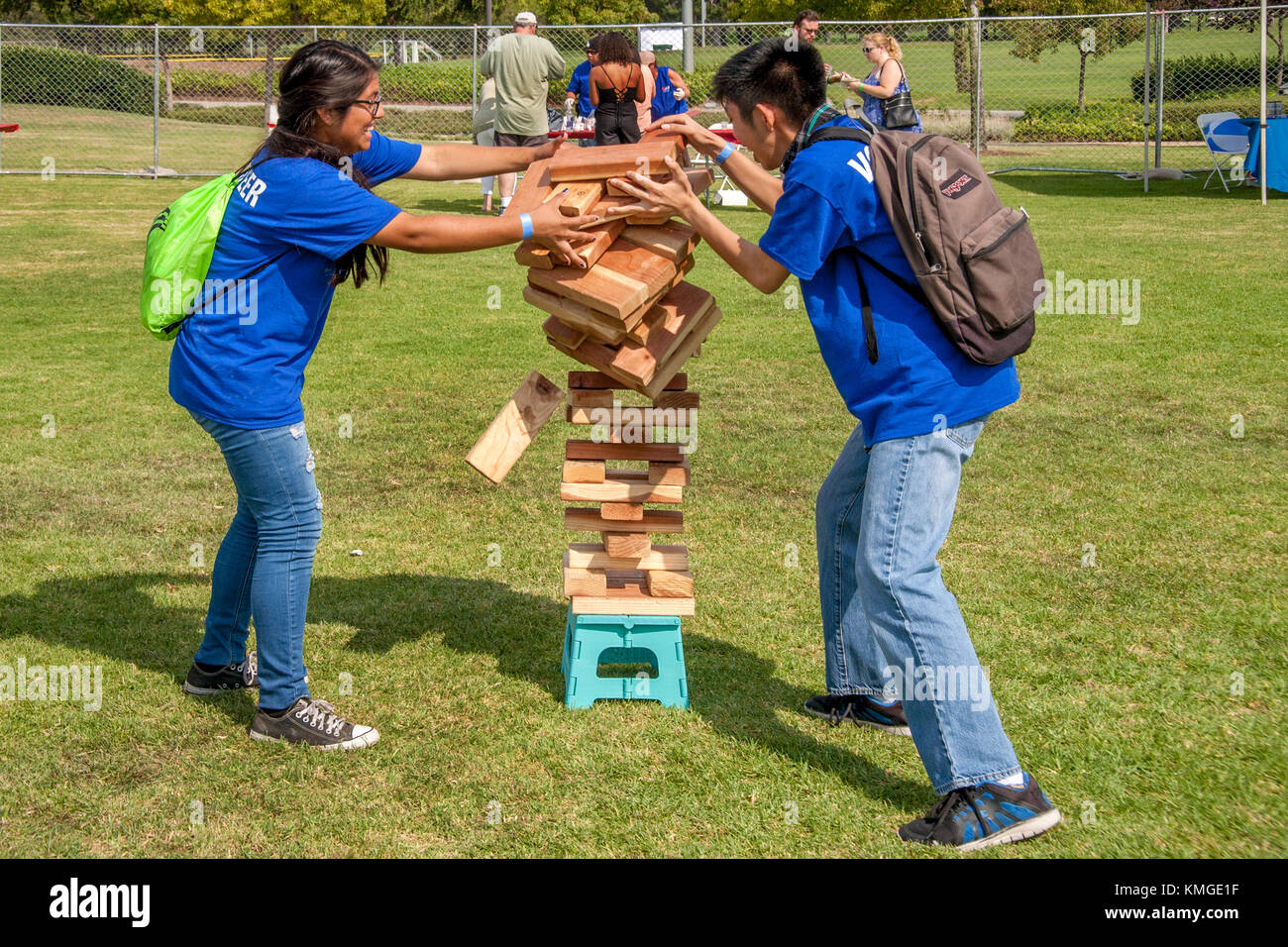 Avente impilati a loro jenga gigante pila un po' troppo alta, due americani  asiatici ragazzi cercare di catturare la caduta dei blocchi di legno in un  festival all'aperto in fountain valley, ca