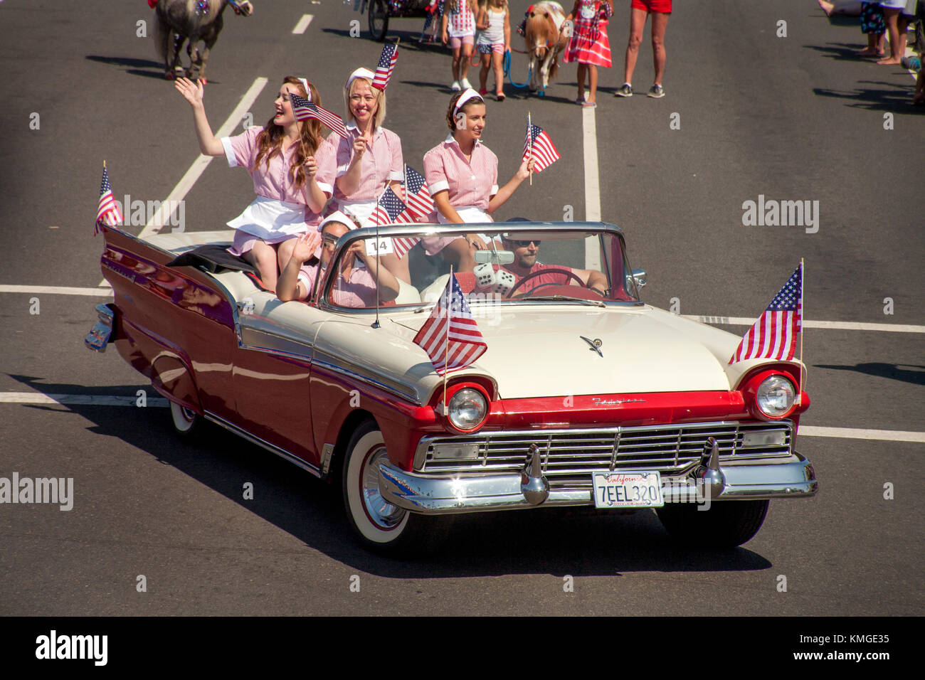 Partecipando a un 4 luglio sfilata in Huntington Beach, CA, esuberante cameriere locali ci onda bandiere da un 1958 Ford Fairlane 500 skyliner convertibile. (Foto di spencer grant) Foto Stock