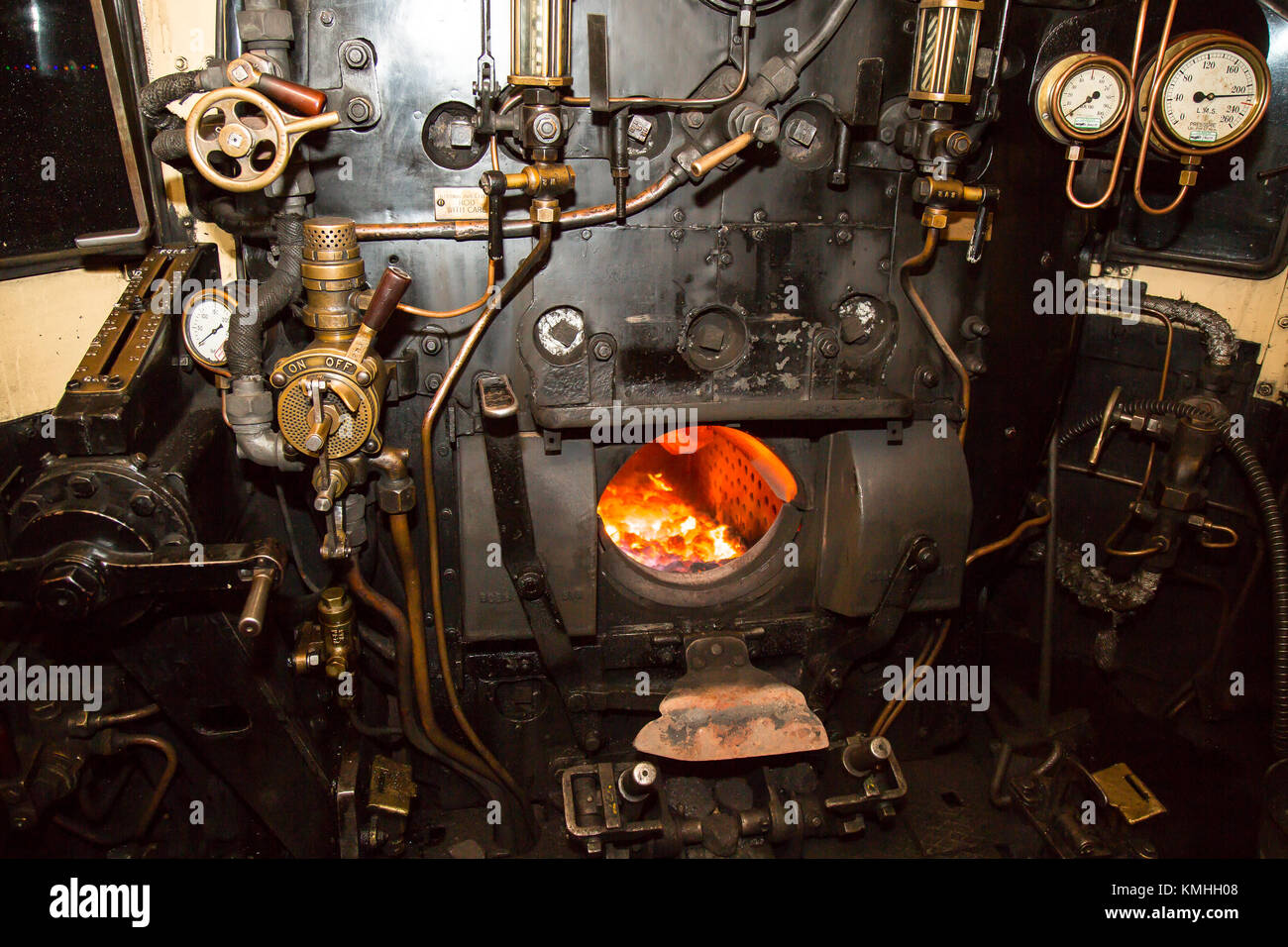 Colpo notturno all'interno della cabina della locomotiva a vapore, guardando nella camera antincendio illuminata della piastra posteriore della caldaia. Valvole, aste, tubi, manometri. Foto Stock