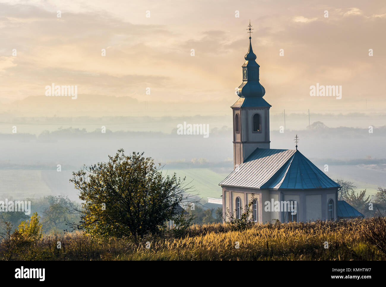 Chiesa su una collina sopra il nebuloso valle rurale al tramonto. incantevole autunno uno scenario paesaggistico Foto Stock