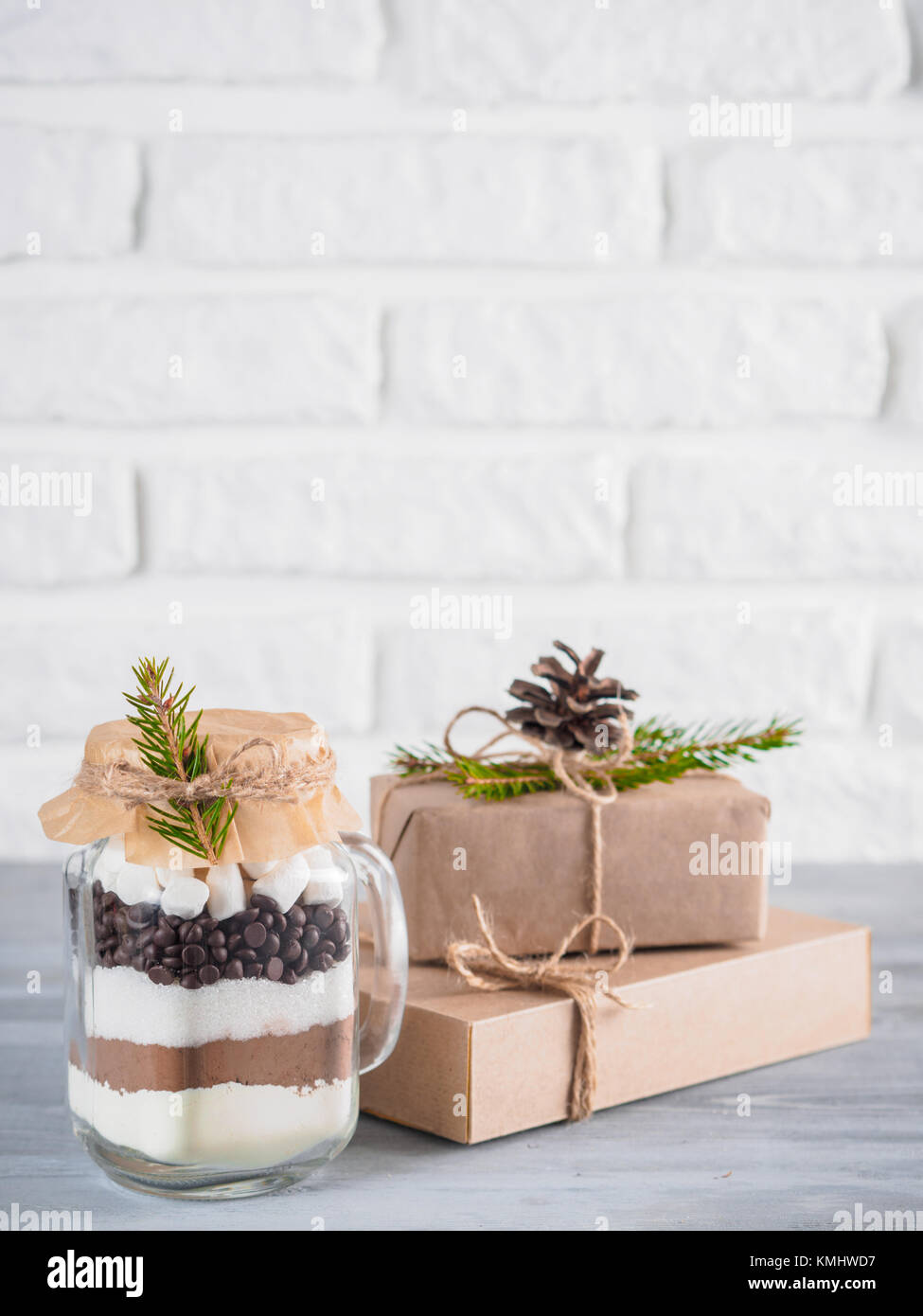 Cioccolata calda mix a mason jar e rustico confezioni regalo sulla tabella di colore grigio e bianco muro di mattoni. Natale e vacanze inverno budget-friendly doni idea. Copia Foto Stock