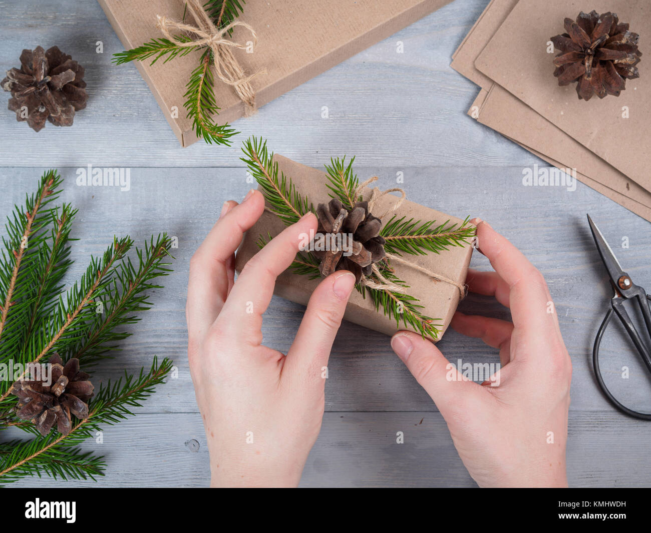 Mani femminili dare avvolto vacanze di Natale fatti a mano presente nella carta craft. Rami di abete rosso e gli strumenti su grigio tavolo in legno. Vista superiore.Workplace per pr Foto Stock