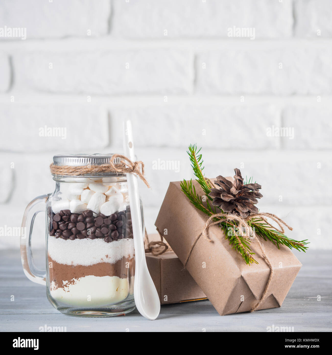 Cioccolata calda mix a mason jar e rustico confezioni regalo sulla tabella di colore grigio e bianco muro di mattoni. Natale e vacanze inverno budget-friendly doni idea. Copia Foto Stock