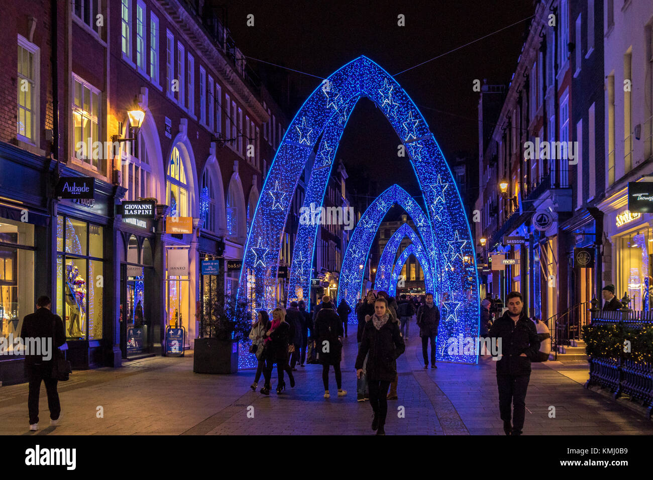 Le persone che camminano lungo South Moulton St a Natale, che è stato decorato con grandi archi blu di Natale, Londra, Regno Unito Foto Stock