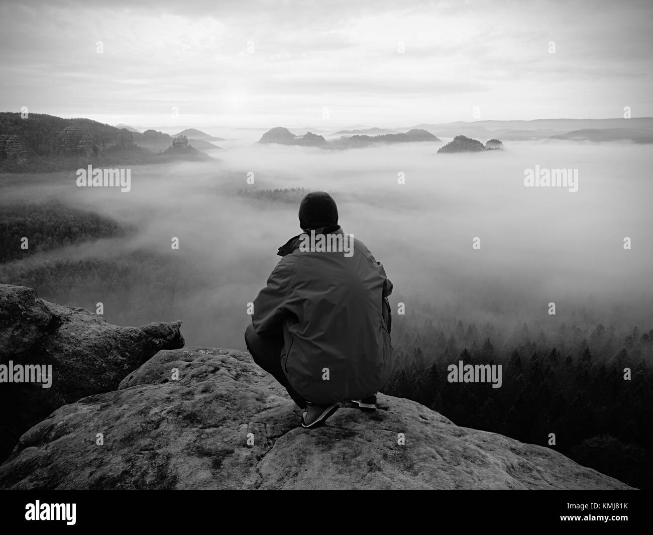 Escursionista su uno sperone roccioso a picco. Splendida alba in montagna, pesante nebbia cremosa nella profonda valle. L'uomo al vertice. Foto in bianco e nero. Foto Stock
