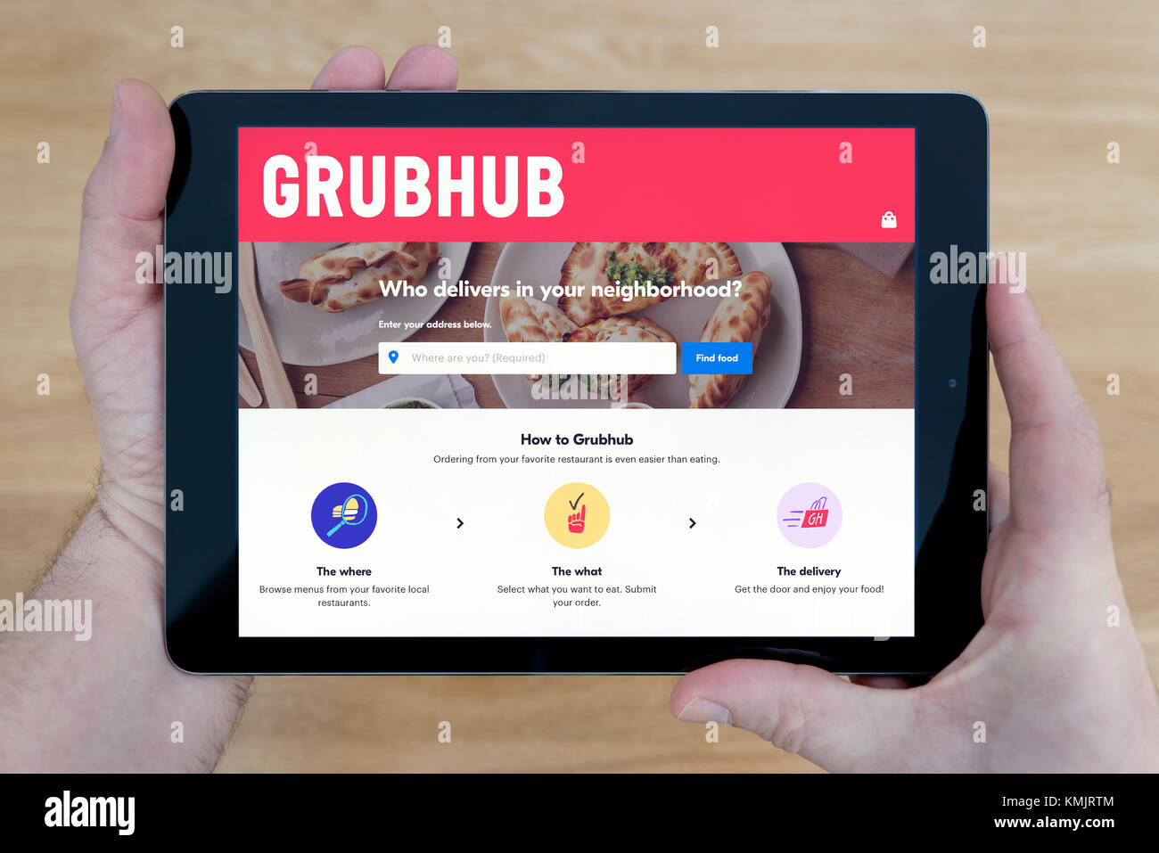 Un uomo guarda il sito Grubhub sul suo iPad dispositivo tablet, sparato contro un tavolo di legno top sfondo (solo uso editoriale) Foto Stock