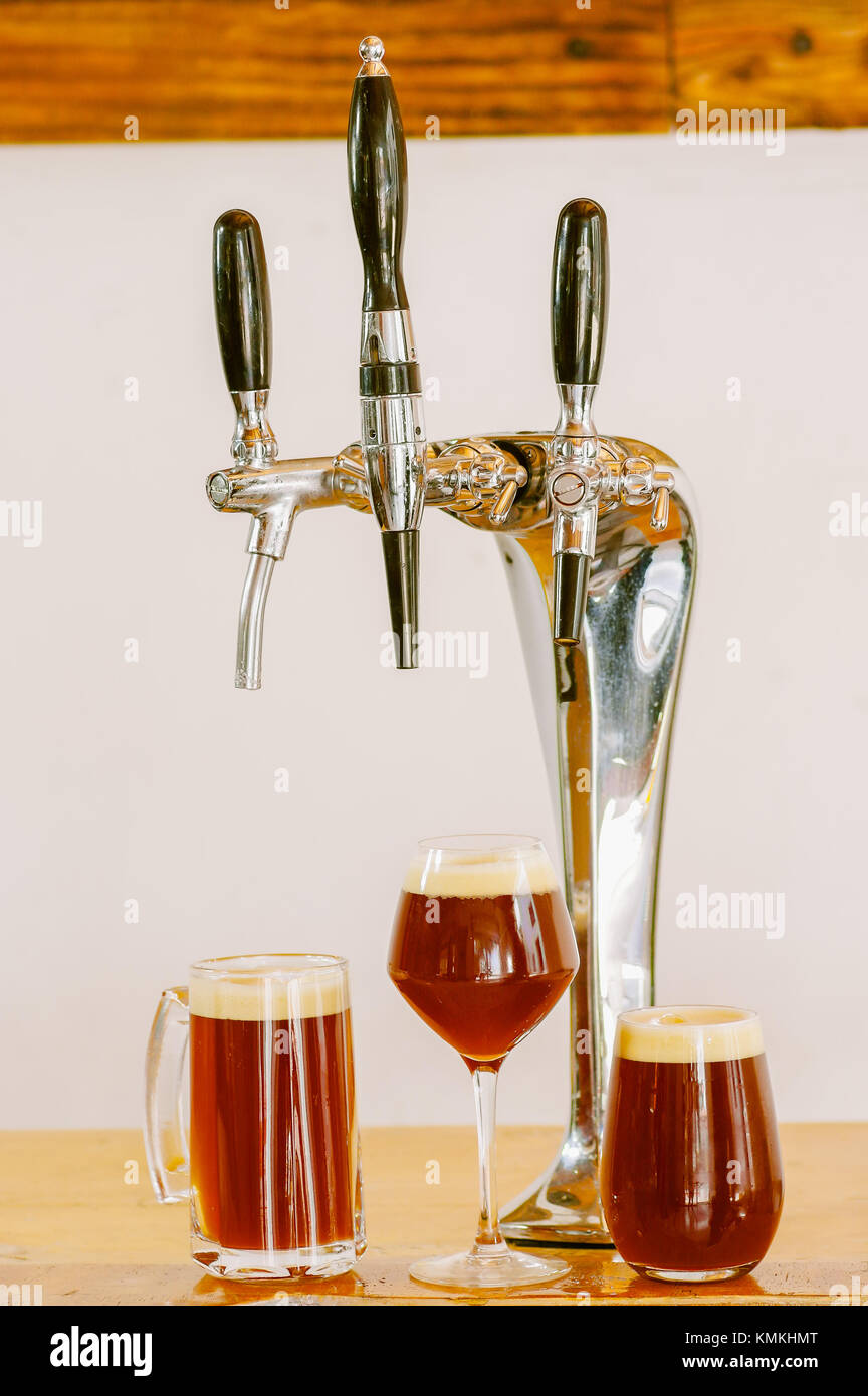 Close up di più rubinetti di birra si trova su un tavolo di legno con alcuni bicchieri pieni di birra, in uno sfondo sfocato Foto Stock