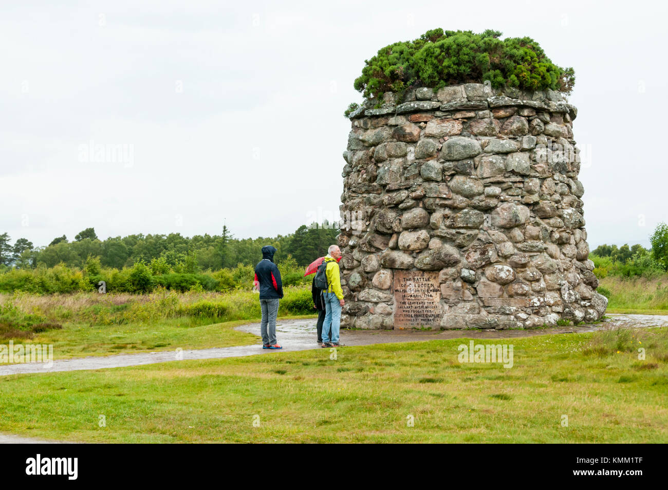 Turisti sotto la pioggia di ispezionare il Memoriale eretto nel 1881 sul campo di battaglia di Culloden. Foto Stock