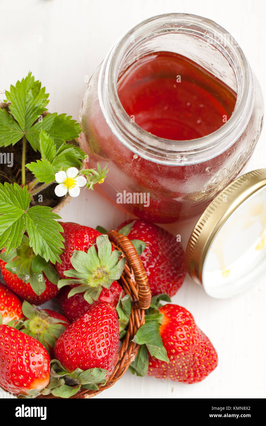 Basker di fragole fresche, germoglio di fiore e un vaso di miele sul tavolo bianco Foto Stock