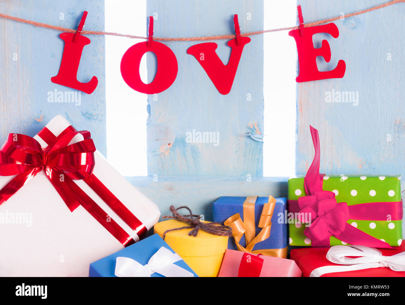 Amore scritte da carta rossa lettere e legato a una stringa con clip in legno su un blu staccionata in legno e una abbondanza di multicolor confezioni regalo. Foto Stock