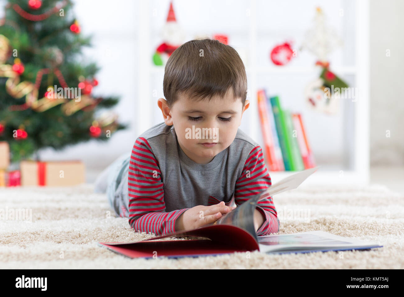 Carino bambino ragazzo leggendo un libro nella parte anteriore dell'albero di Natale, tempo di Natale Foto Stock
